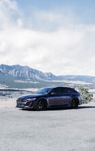 A shiny rental car parked in front of a scenic mountain view.