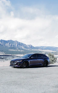 A sleek rental car parked beside a scenic highway with mountains in the background.