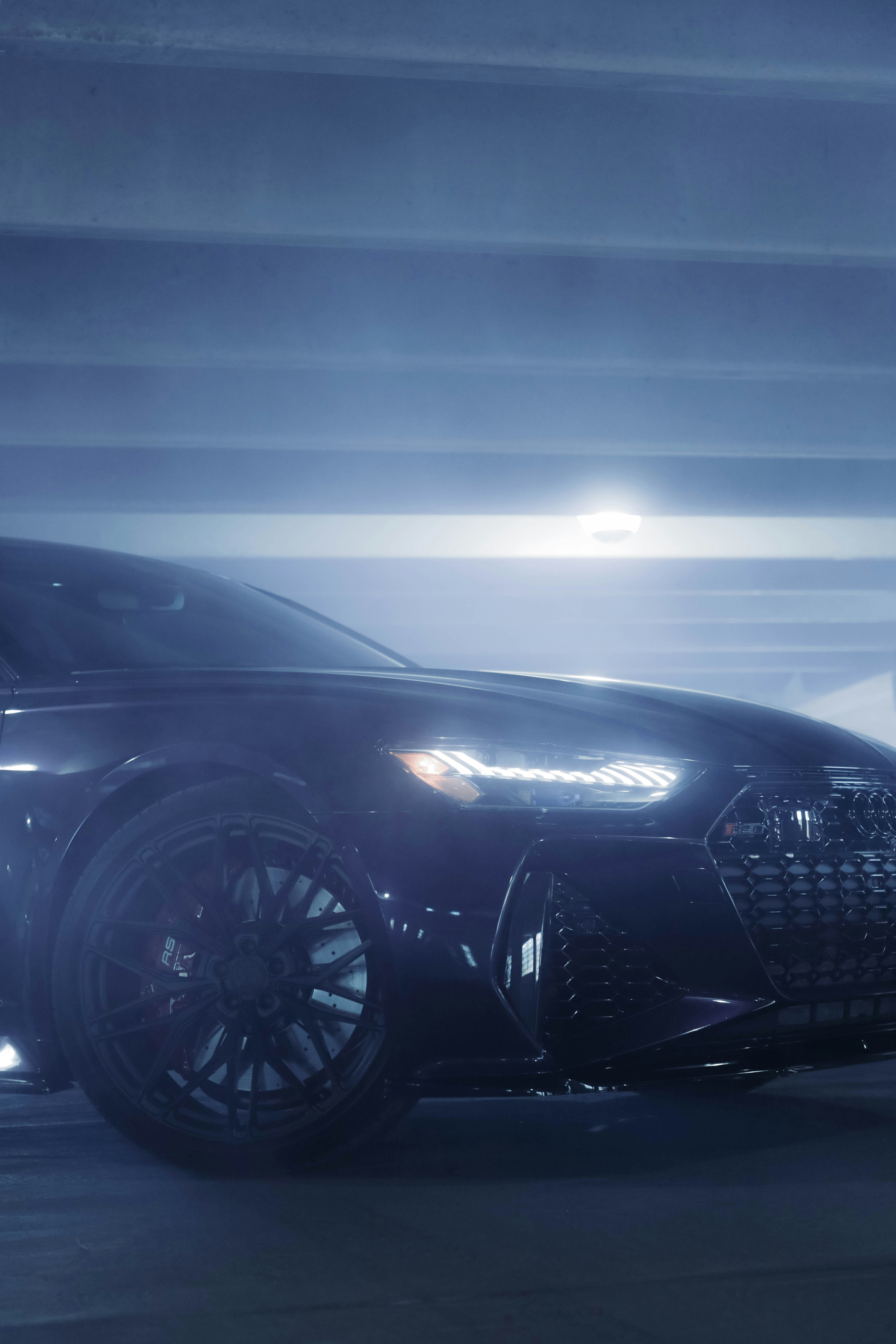 A sleek, modern car is parked in a dimly lit garage. The focus is on the front side of the car, showcasing its shiny, polished surface and distinctive LED headlights. The image captures the elegant design of the car, emphasizing the intricate pattern of the wheel and grill.