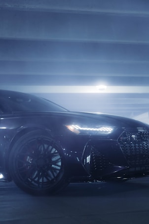 A sleek, modern car is parked in a dimly lit garage. The focus is on the front side of the car, showcasing its shiny, polished surface and distinctive LED headlights. The image captures the elegant design of the car, emphasizing the intricate pattern of the wheel and grill.