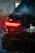 A close-up of a car's rear end with illuminated red taillights, partially enveloped in smoke. The vehicle features sleek, dark paintwork and a visible exhaust pipe. A license plate is partially visible.