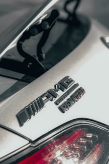 Close-up of the rear portion of a car featuring the AMG and Renntech badges. The image showcases the detail and texture of the car's surface, with a hint of the taillight at the bottom.