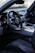 The interior of a luxury car featuring a sleek dashboard with multiple circular air vents, a leather-wrapped steering wheel with a prominent logo in the center, and a digital display screen. The seating is upholstered in high-quality black leather with visible stitching.