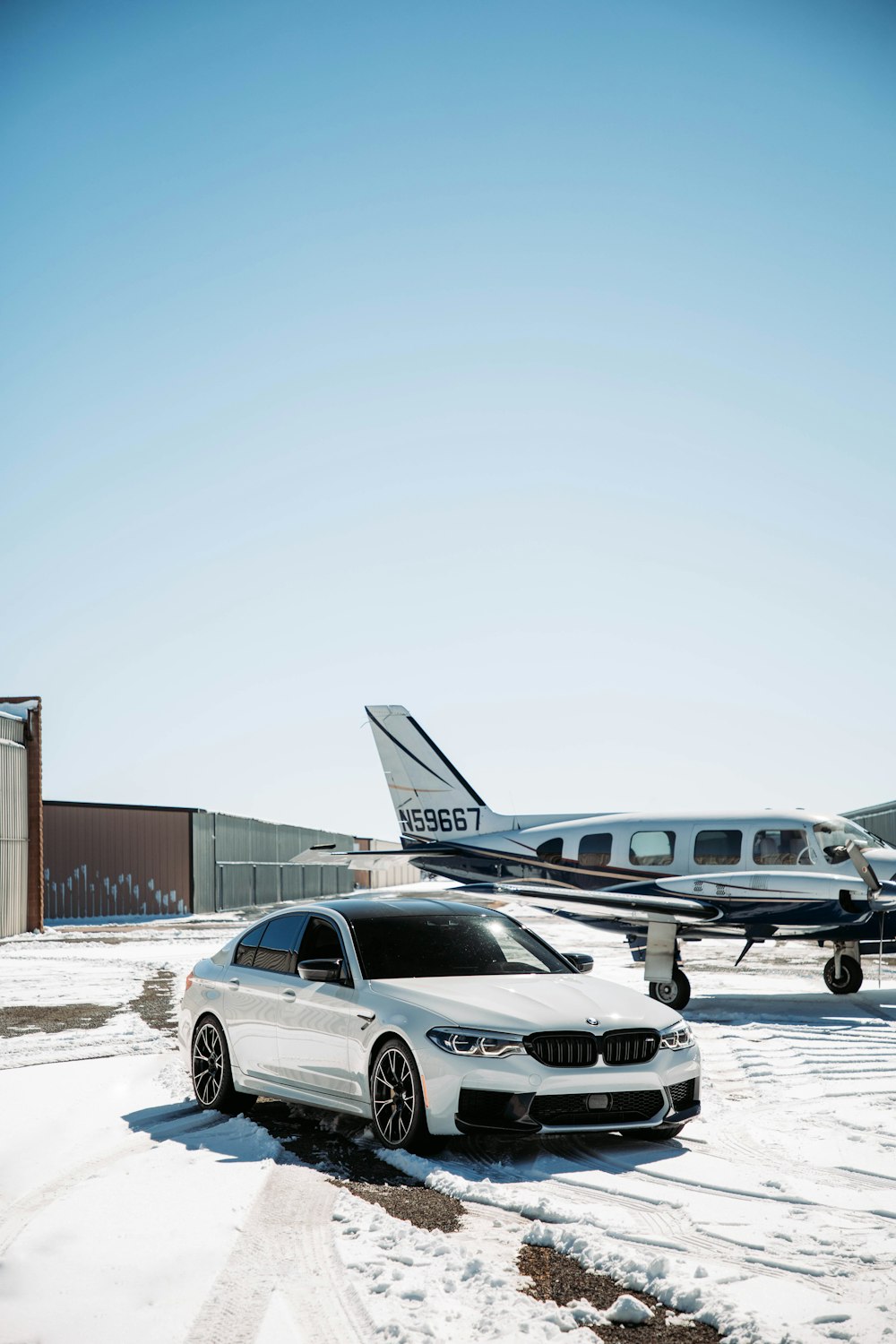 a white car parked next to an airplane on a snowy runway