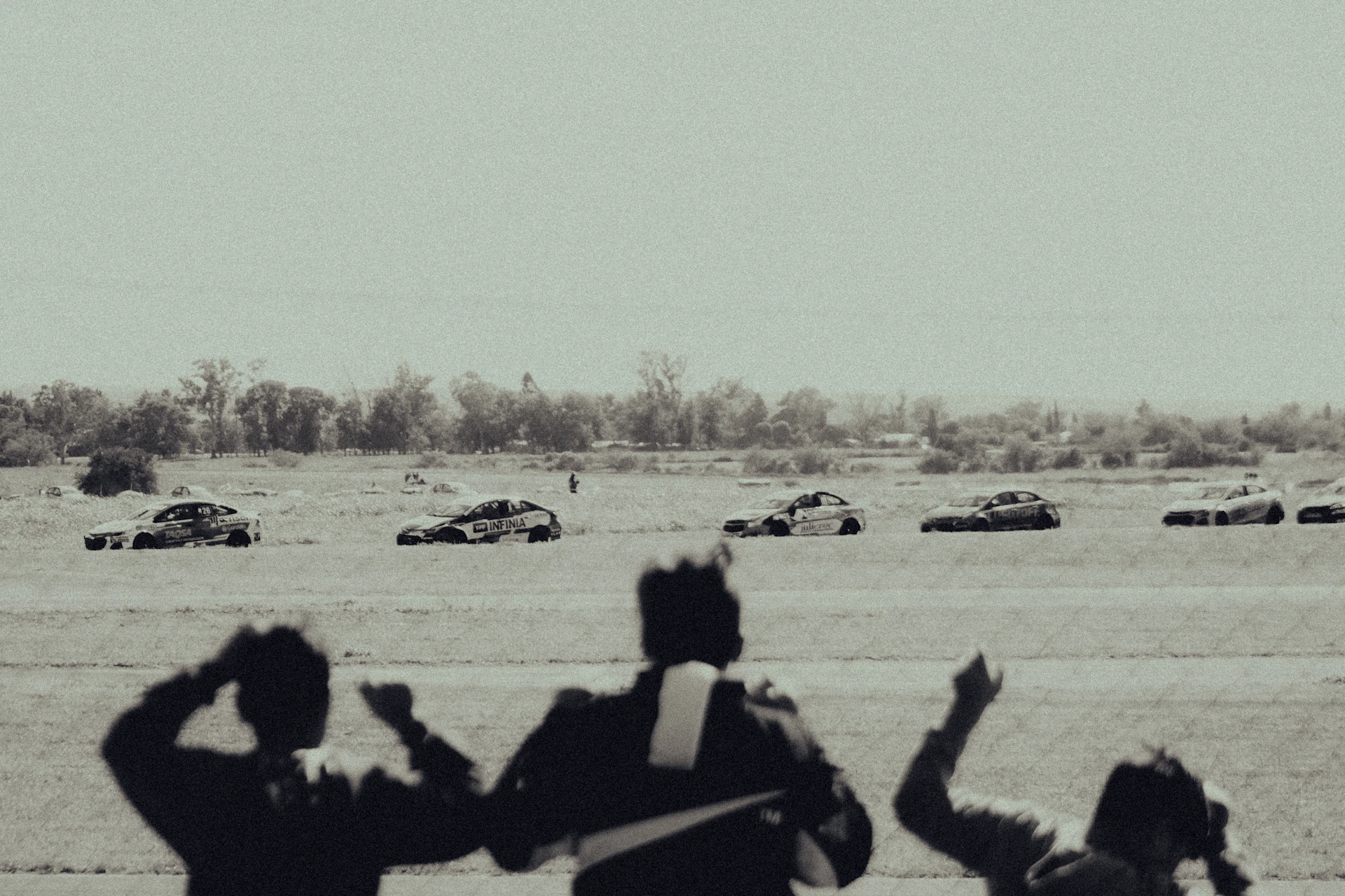 Dynamic image capturing a group of cars lined up at a motorsport event with enthusiastic spectators in the background.