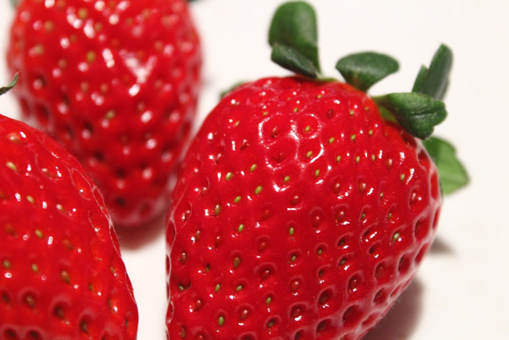 a close up of three strawberries on a white surface