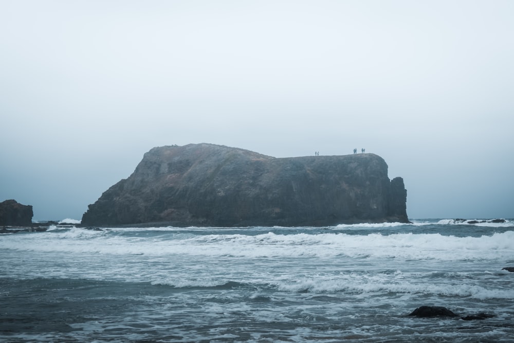 two people standing on a rock in the ocean