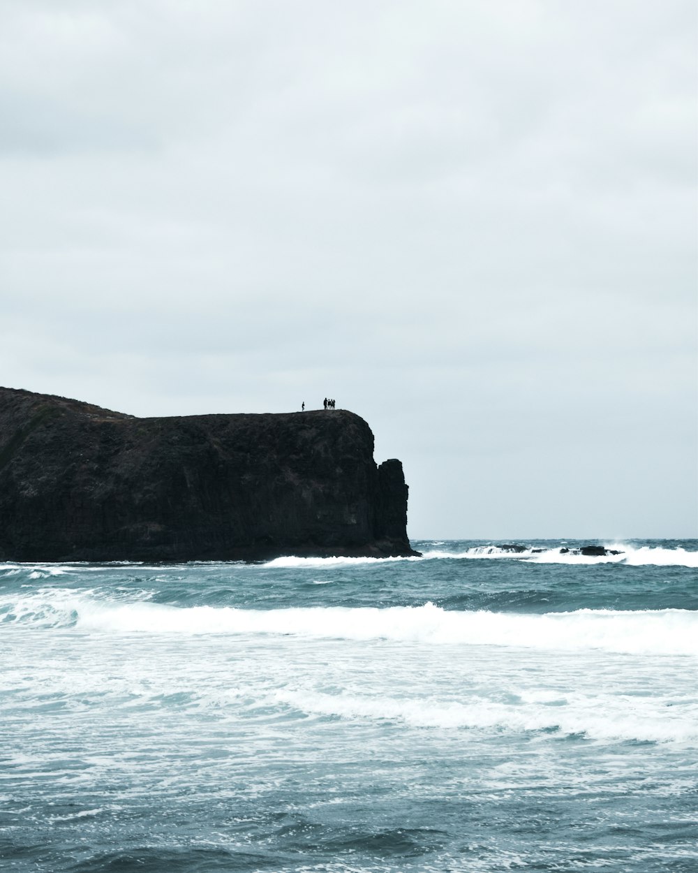 a couple of people standing on top of a cliff near the ocean