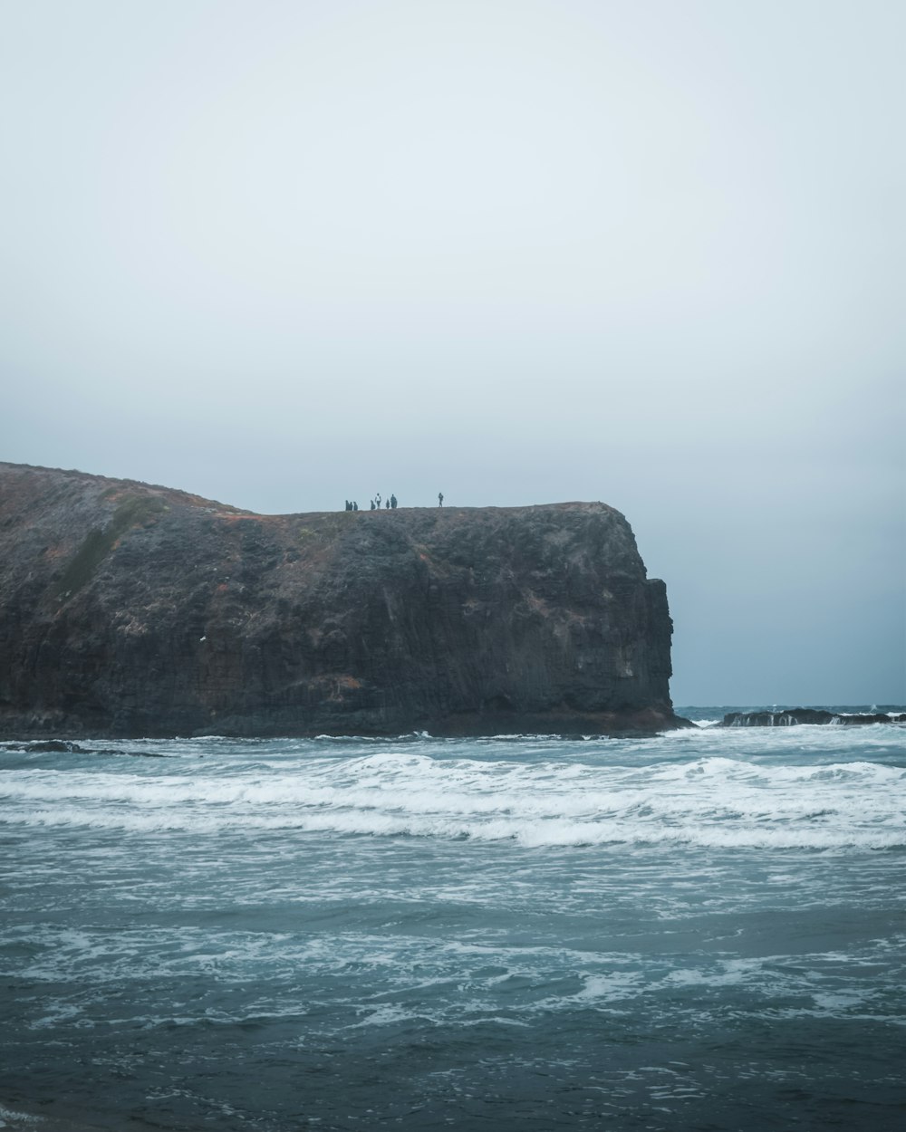 a group of people standing on top of a cliff near the ocean