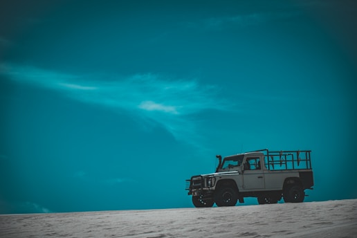 A rugged off-road vehicle is parked on a sandy terrain, silhouetted against a vast, clear teal sky. The landscape suggests an open and remote location, emphasizing the vehicle's capability for adventure and exploration.