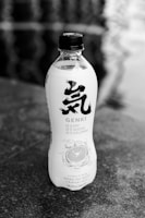 A plastic bottle with a black cap, featuring stylized black text on the label. The label includes nutritional information highlighting zero fat, sugar, and calories. It is branded as a citrus-flavored sparkling water, with an illustration of a lemon slice and water splash.