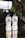 Two bottles of Genki sparkling water are placed on a reflective surface. The left bottle is citrus flavored, and the right one is peach flavored. Both bottles have a simple design with bold Japanese characters and are set against a softly blurred background of green leafy plants and a modern interior.