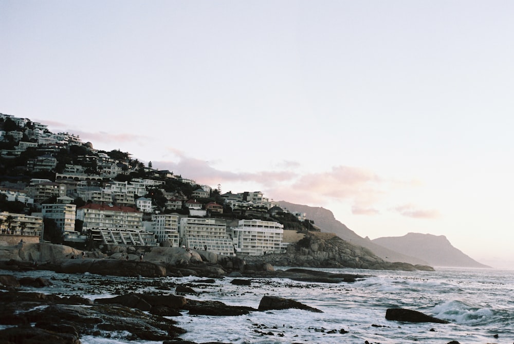 a view of a rocky beach with houses on a hill in the background