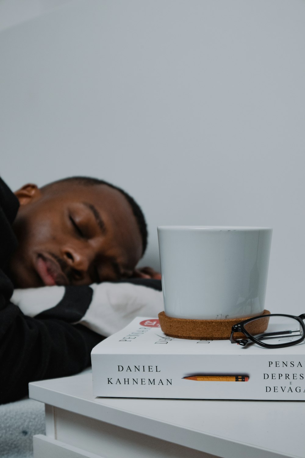 a man sleeping on top of a stack of books next to a cup of coffee