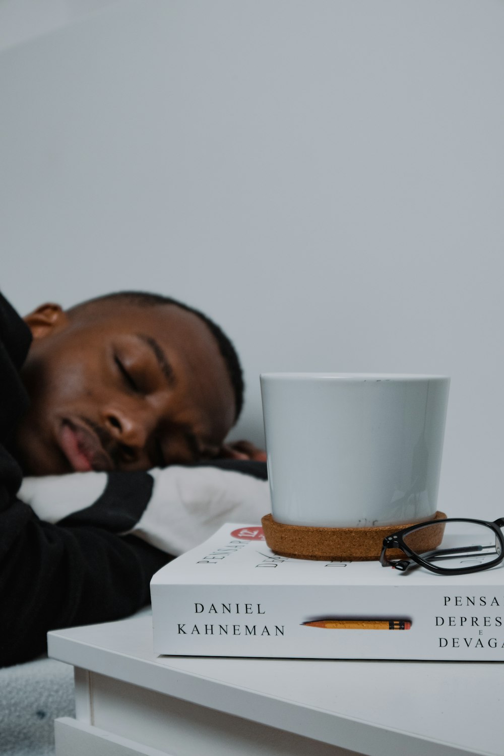 Un hombre durmiendo encima de una pila de libros junto a una taza de café