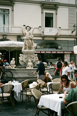 a group of people sitting at tables in front of a fountain