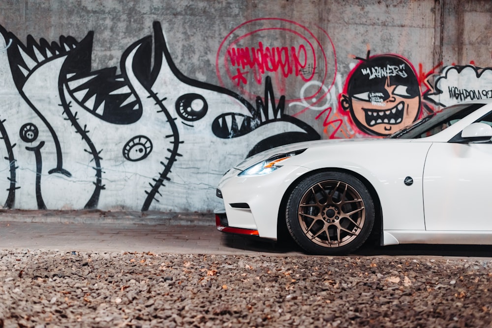 a white sports car parked in front of a graffiti covered wall