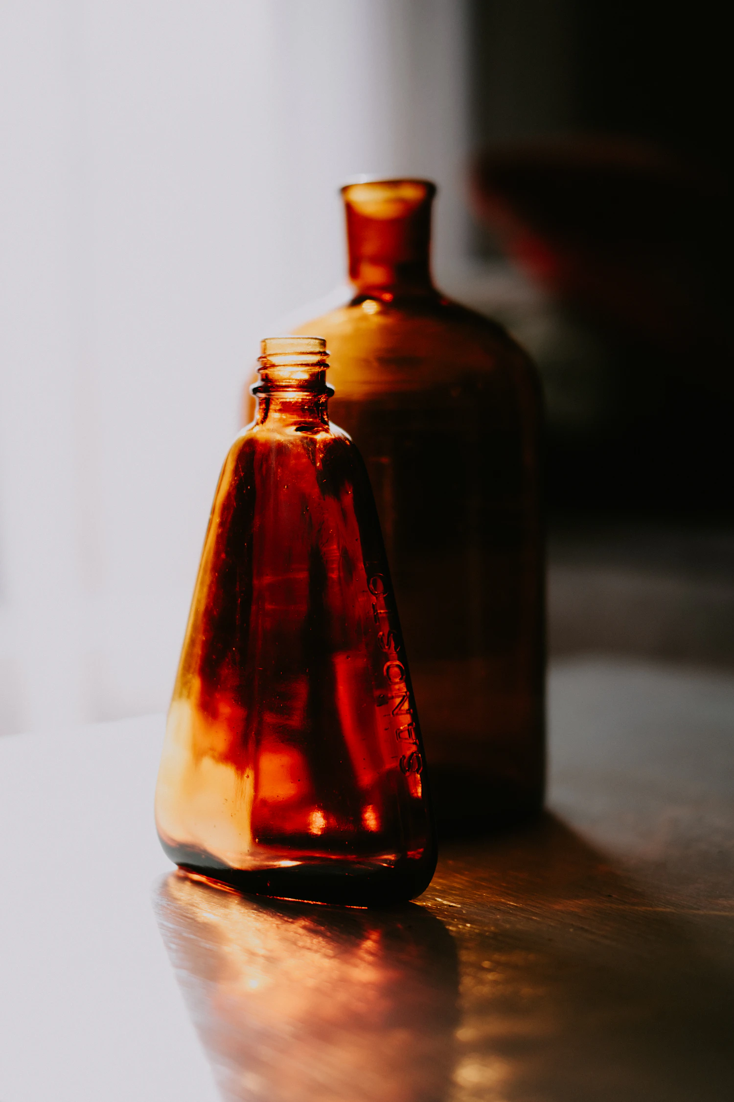 An amber glass bottle throwing a long warm reflection across a table