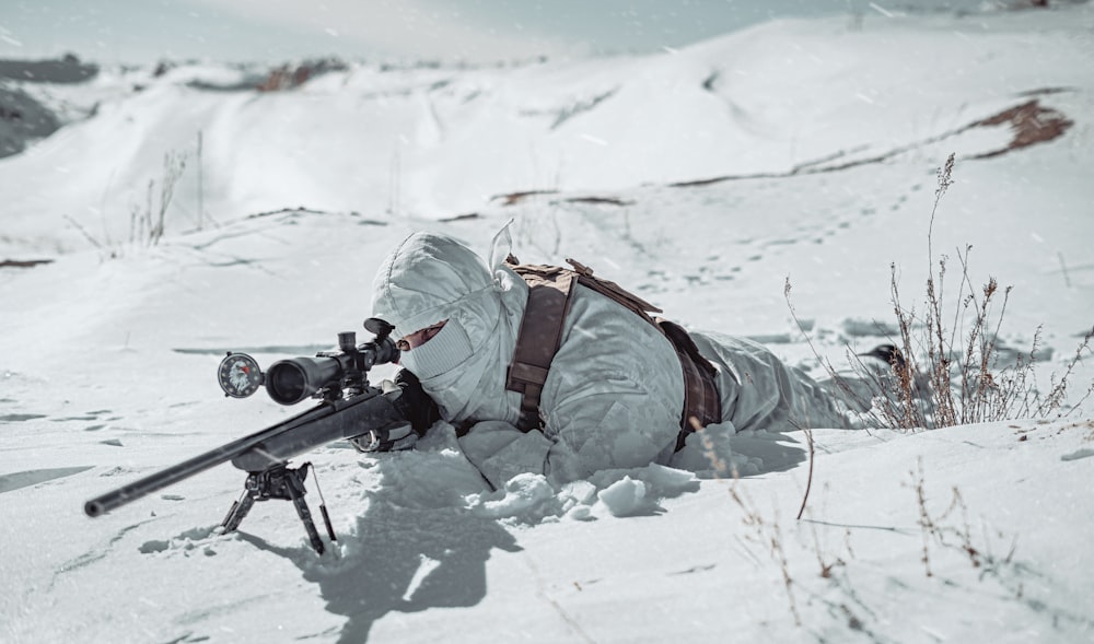 a man laying in the snow with a rifle