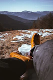 A rugged hiking boot stepping through pristine snow with wildroar branded winter socks visible above the cuff against a backdrop of jagged mountains.