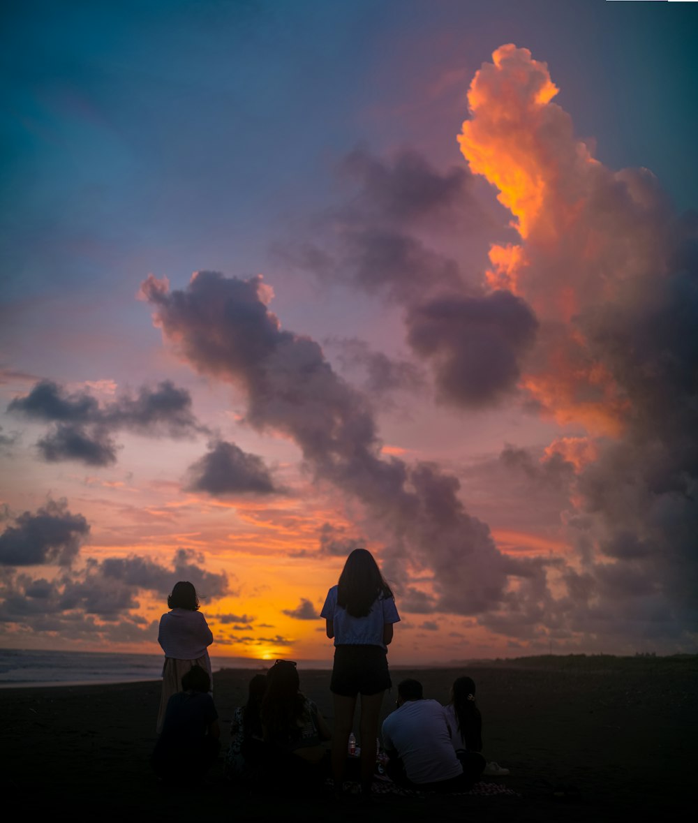 a group of people sitting on top of a beach under a cloudy sky