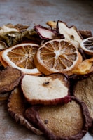 A close-up view of various dried fruit slices, including oranges, apples, and others. The texture of the dried fruits is rugged with visible details of the fruit's surface and rind. The lighting creates a warm and earthy tone.