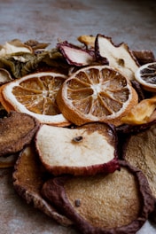 A close-up view of various dried fruit slices, including oranges, apples, and others. The texture of the dried fruits is rugged with visible details of the fruit's surface and rind. The lighting creates a warm and earthy tone.