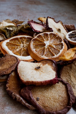 A close-up view of various dried fruit slices, including oranges, apples, and others. The texture of the dried fruits is rugged with visible details of the fruit's surface and rind. The lighting creates a warm and earthy tone.