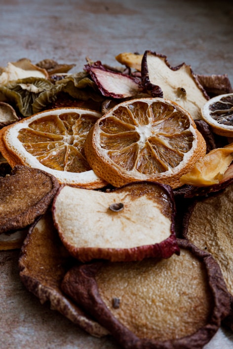 A close-up view of various dried fruit slices, including oranges, apples, and others. The texture of the dried fruits is rugged with visible details of the fruit's surface and rind. The lighting creates a warm and earthy tone.