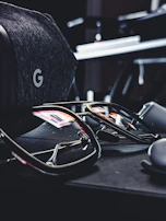 A pair of futuristic smart glasses resting on a dark surface with subtle blue reflections.