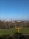 A disc golf basket with chains is situated in an open, grassy field. In the background, there is a large urban skyline with several tall buildings and notable landmarks. The sky above is clear and blue.