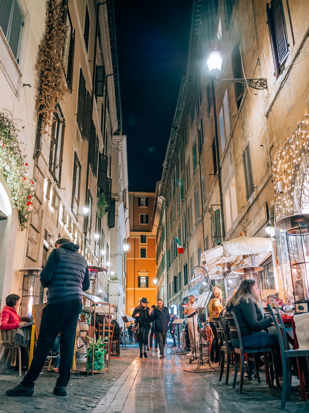 a narrow city street at night with people sitting at tables