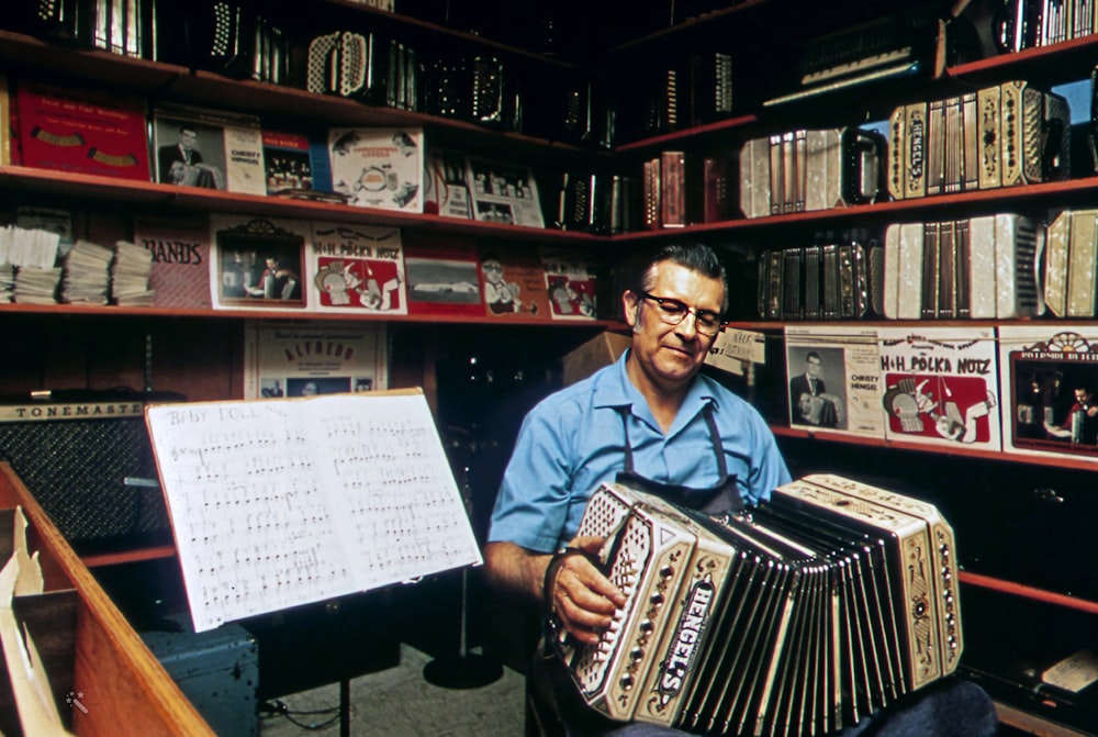 a man sitting in front of a book shelf holding an accordion