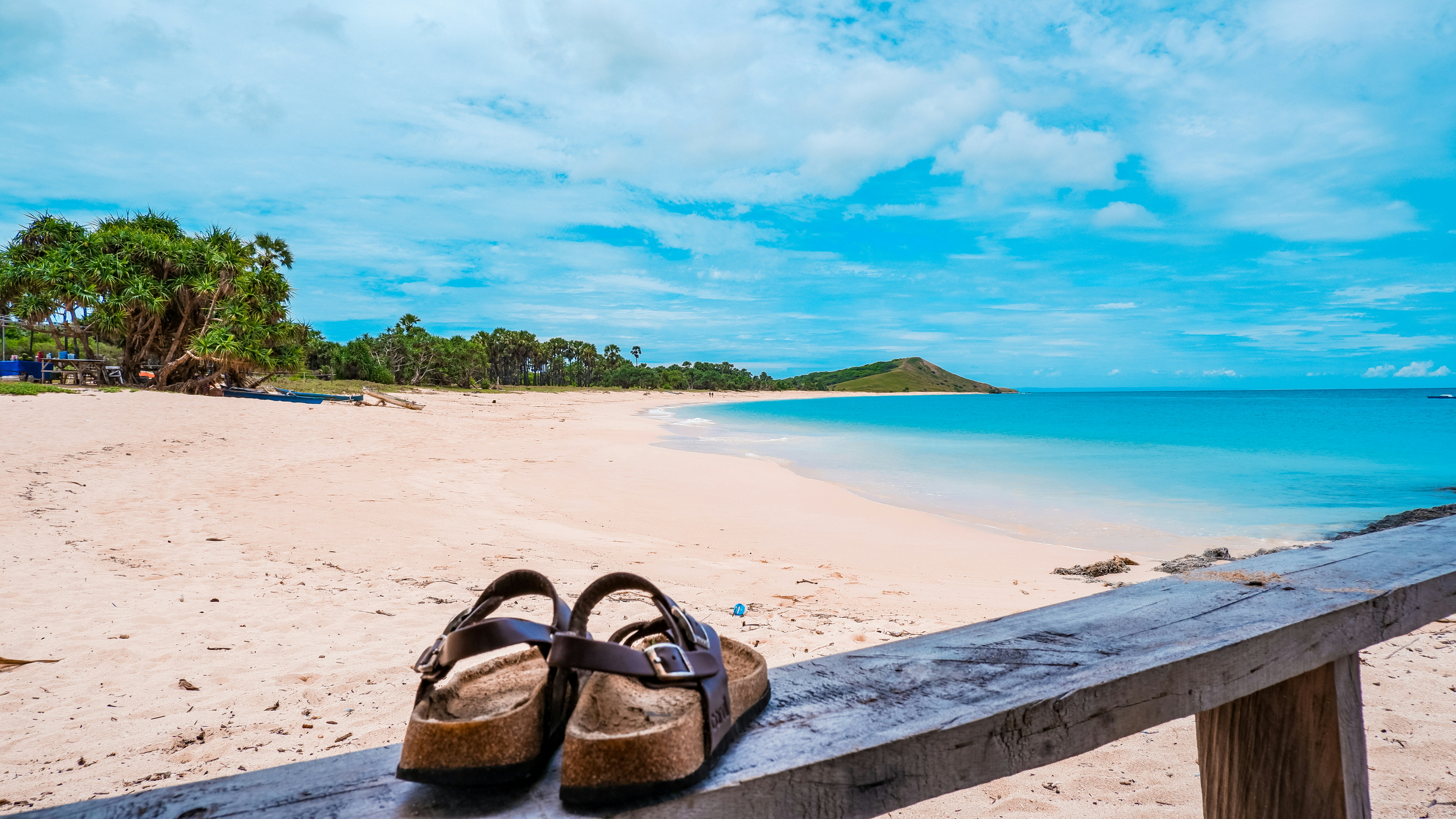 Luxury sandal collection laid on warm sand beach, golden hour light, Mediterranean aesthetic, warm amber tones