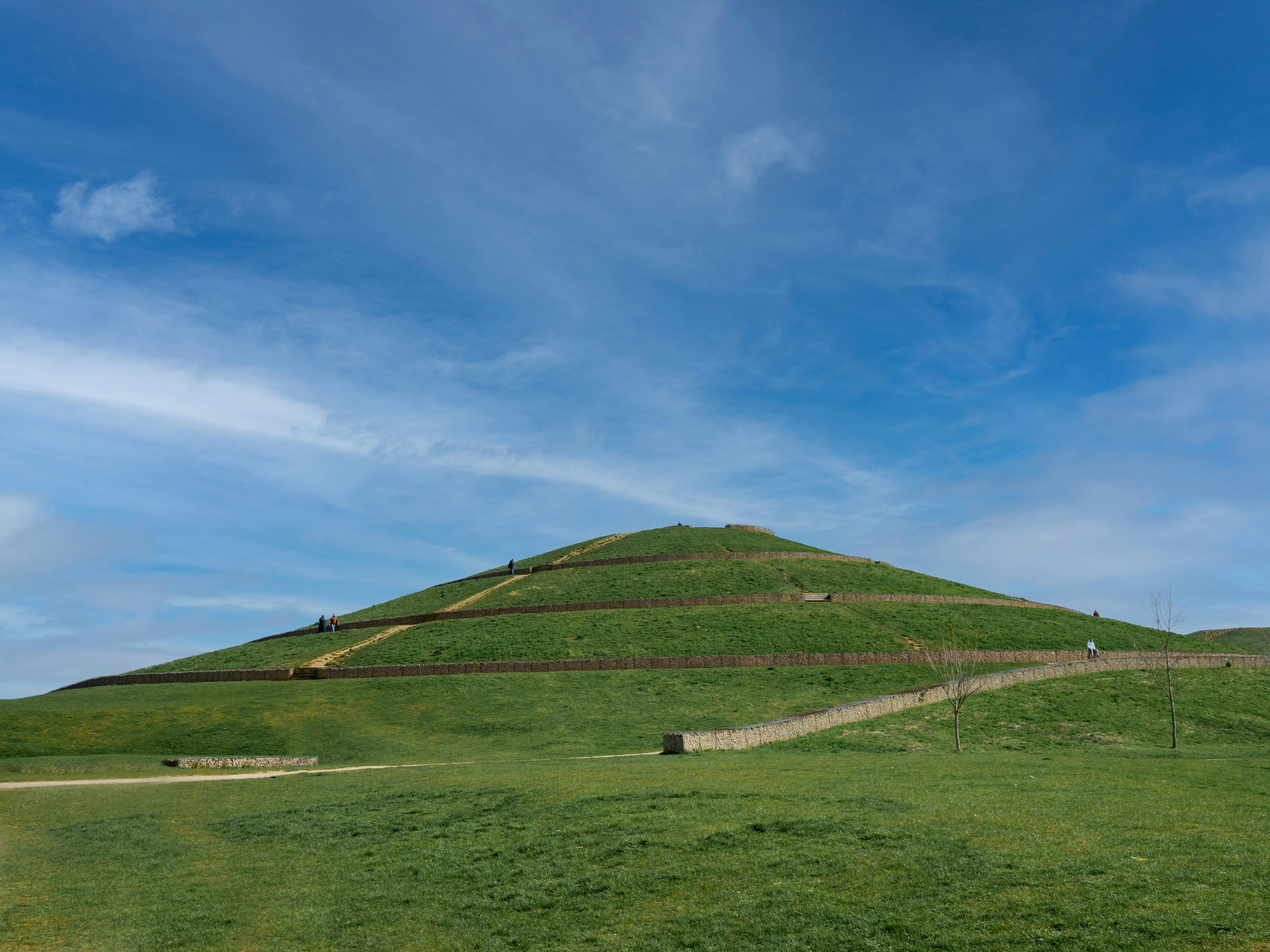 a large grassy hill with a few people walking up it