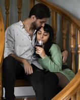 a man and a woman sitting on a wooden chair holding a glass of wine