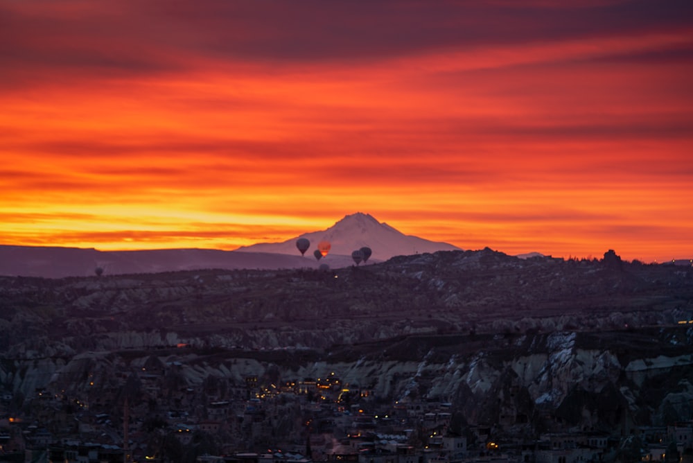 a sunset view of a mountain with hot air balloons in the sky