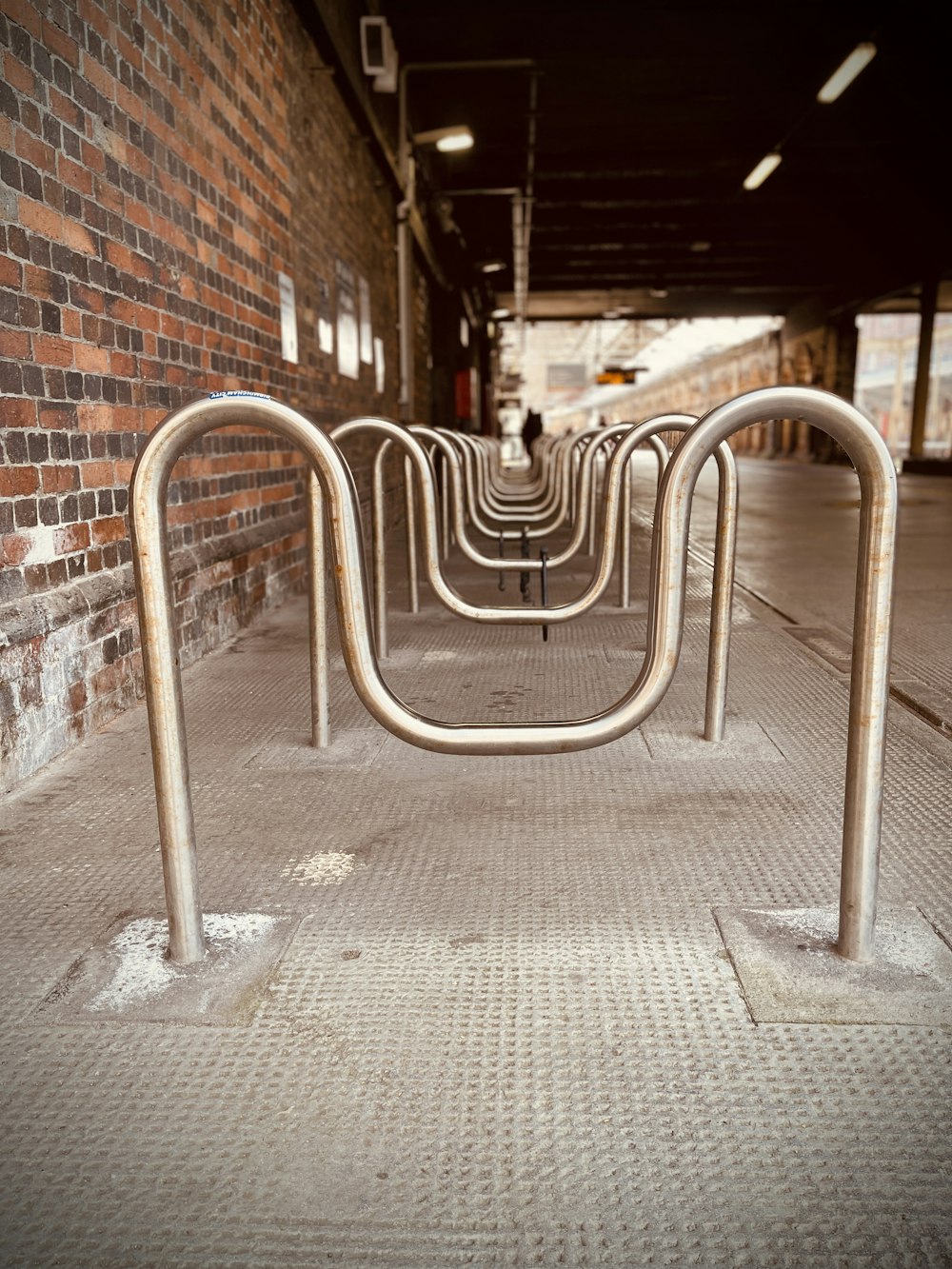 a row of metal bars on a sidewalk next to a brick wall