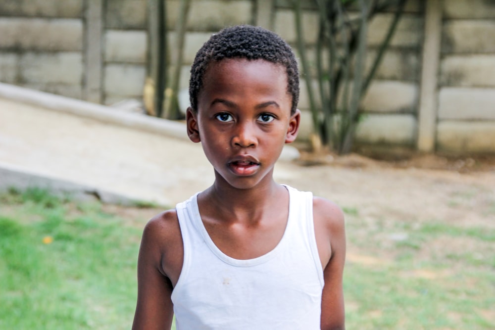 a young boy in a tank top standing in the grass