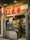 A cozy Asian restaurant storefront with prominent red signage and a glowing neon sign. The entrance includes a glass door, through which interior seating and customers are visible. Various promotional materials and Michelin stickers are displayed, indicating accolades and specialization in handcrafted soybean delicacies. The street sign reads 'Rua da Tercena'.