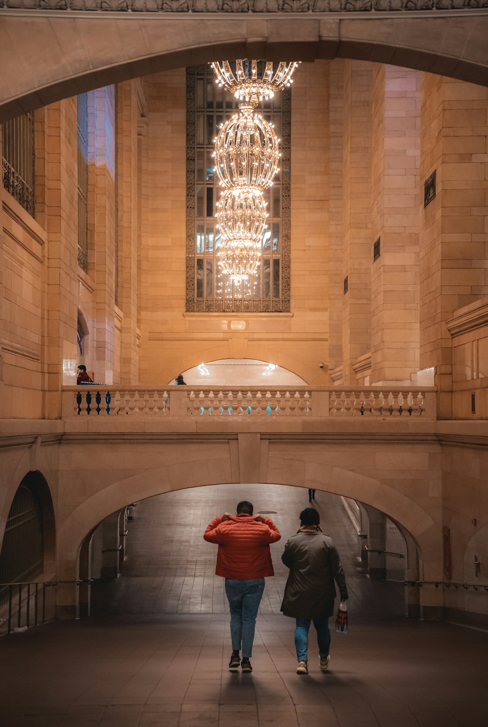 two people walking under a chandelier in a building