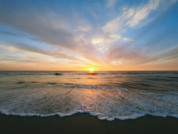 Pôr do sol sobre o mar com ondas chegando à areia