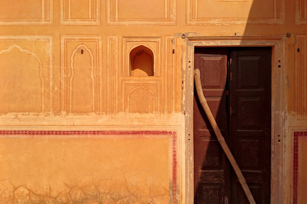 an open door in a yellow wall with a wooden stick sticking out of it