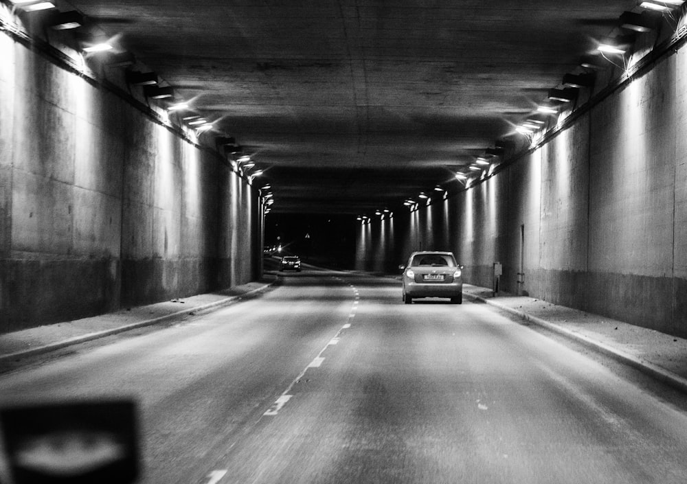 a black and white photo of a car driving through a tunnel