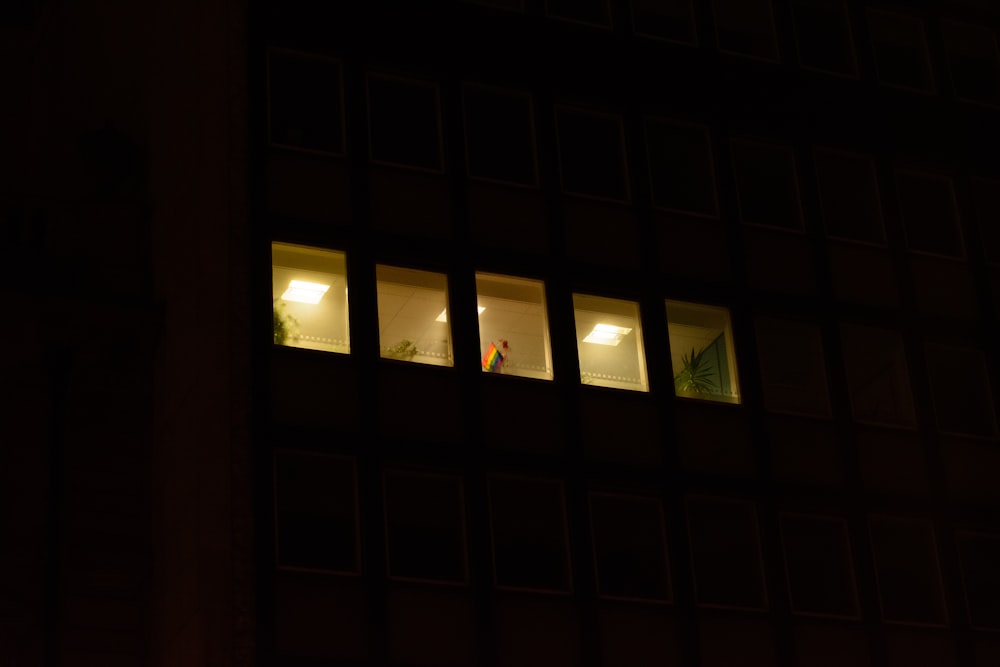 two people standing in the window of a building at night