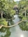 A serene environment featuring a winding water body surrounded by lush green vegetation and trees. There is a building at the far end partially hidden by the foliage, suggesting a peaceful retreat in a natural setting.