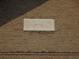 A historic brick wall features an engraved stone plaque. The plaque is inscribed with 'First Brethren Church 1898,' indicating the building's association and the year of its establishment. The bricks are uniformly arranged and vary slightly in color, giving a vintage appearance.