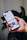 A hand holds a smartphone displaying a social media profile interface app, with text, icons, and images visible on the screen against a blurred plant background.