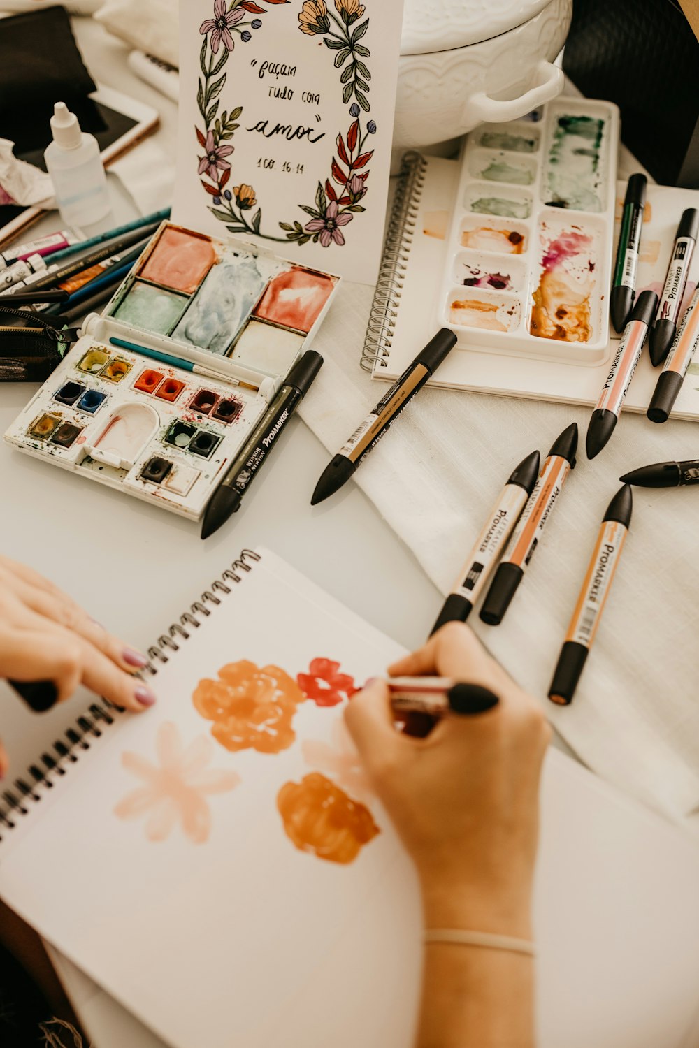 a woman is drawing on a paper with watercolors