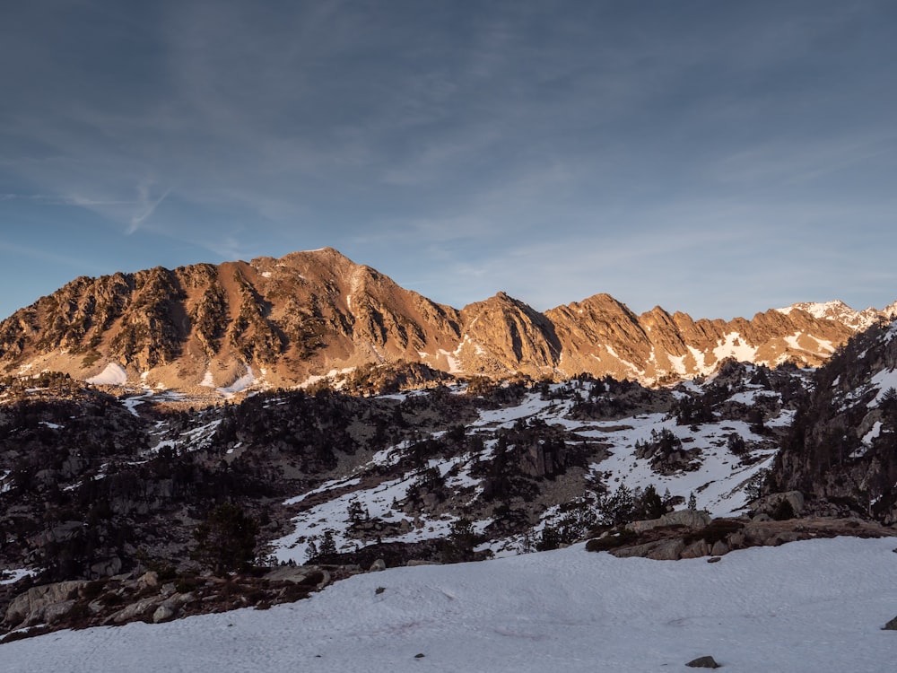 a snow covered mountain range at sunset with a few clouds